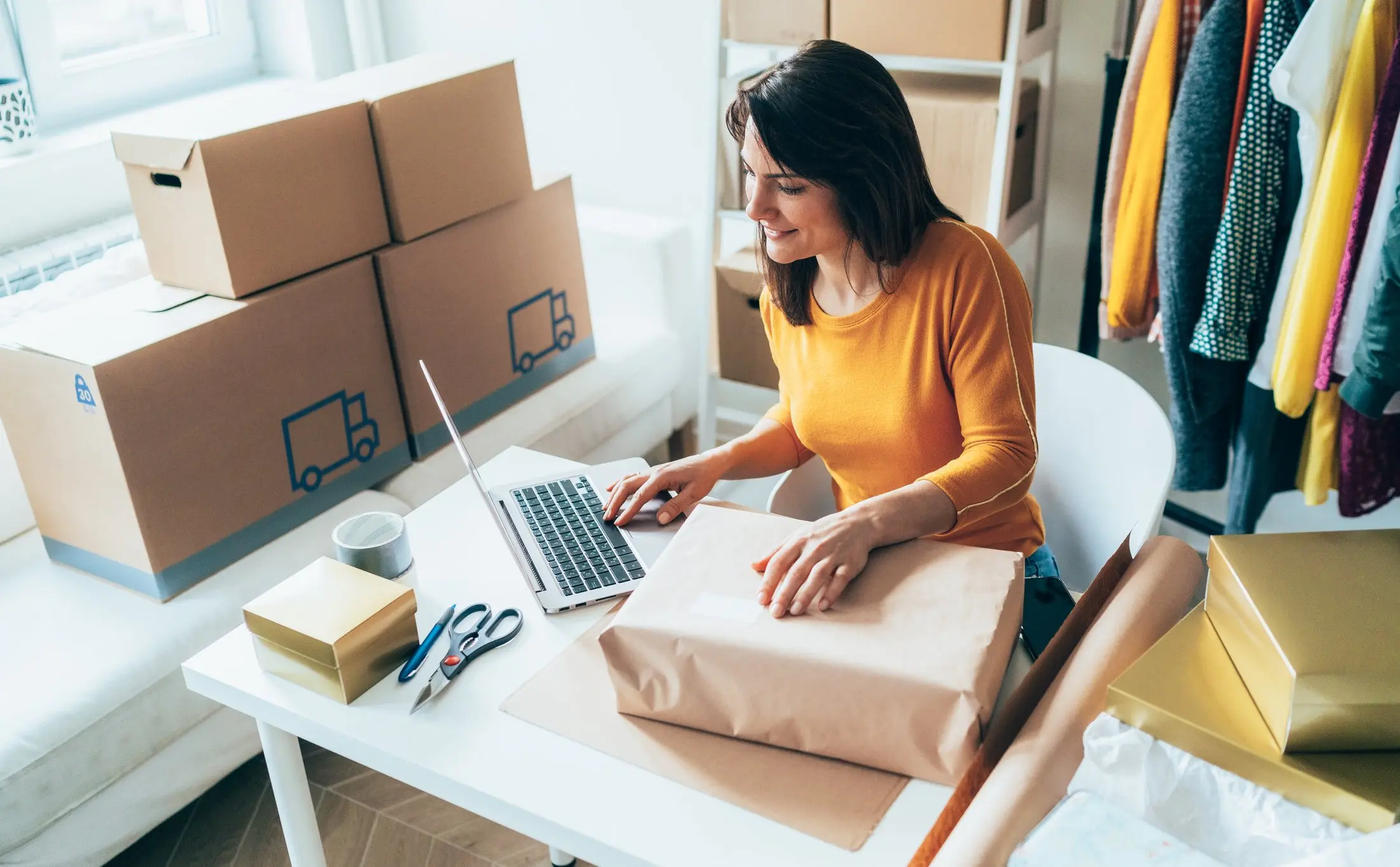 An entrepreneur sitting at a desk managing shipping, processing orders, and packing boxes.