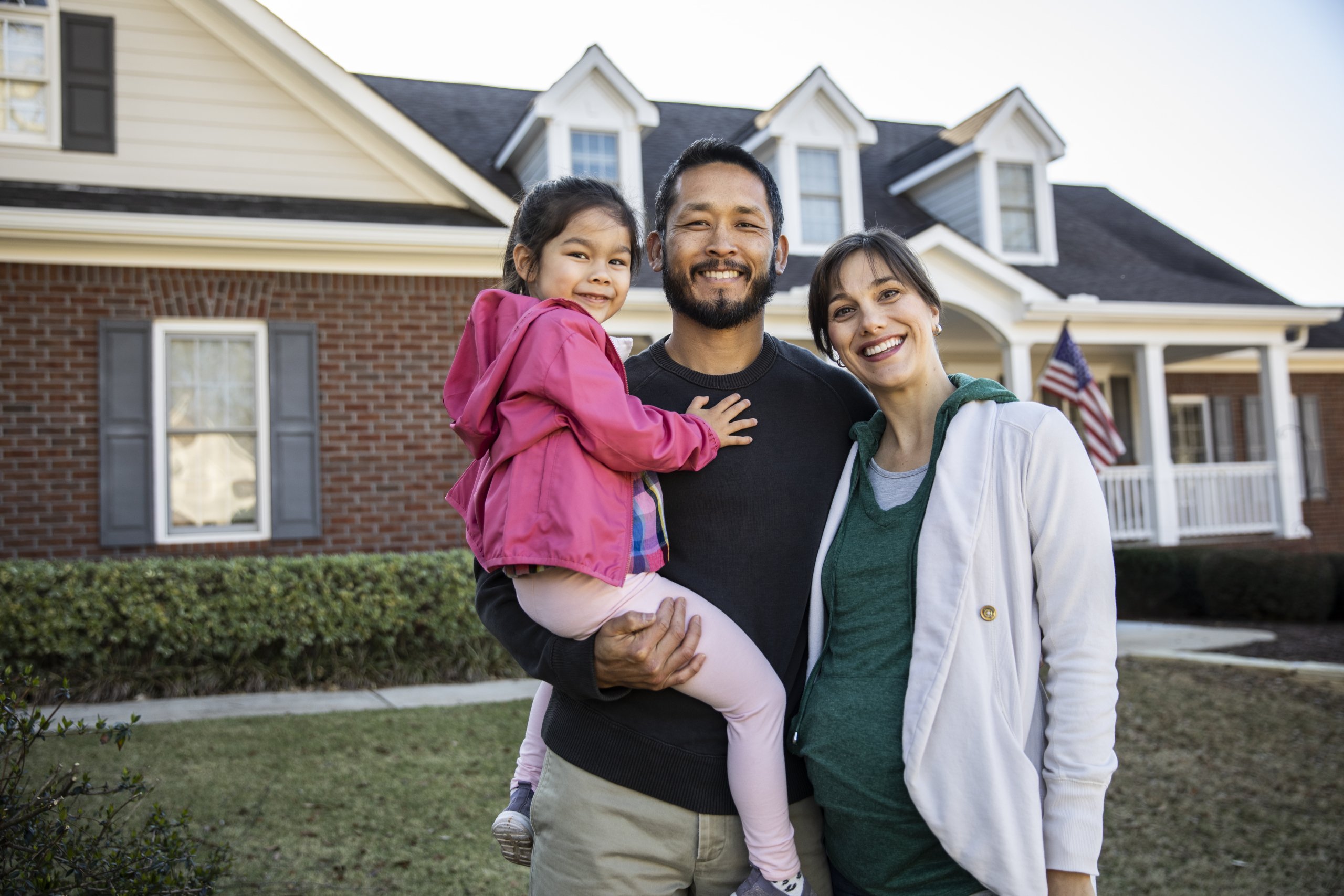 A smiling family of three standing in front of their new home, which is a type of collateral.
