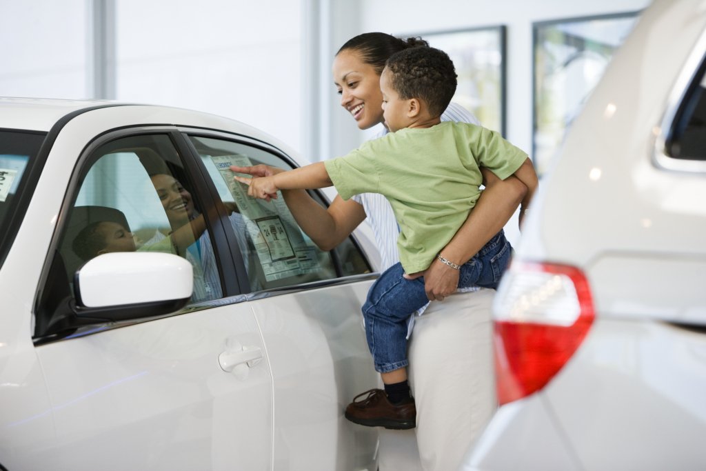 A mother holding her and son looking at the type of features on a new car she is considering purchasing with an auto loan. 