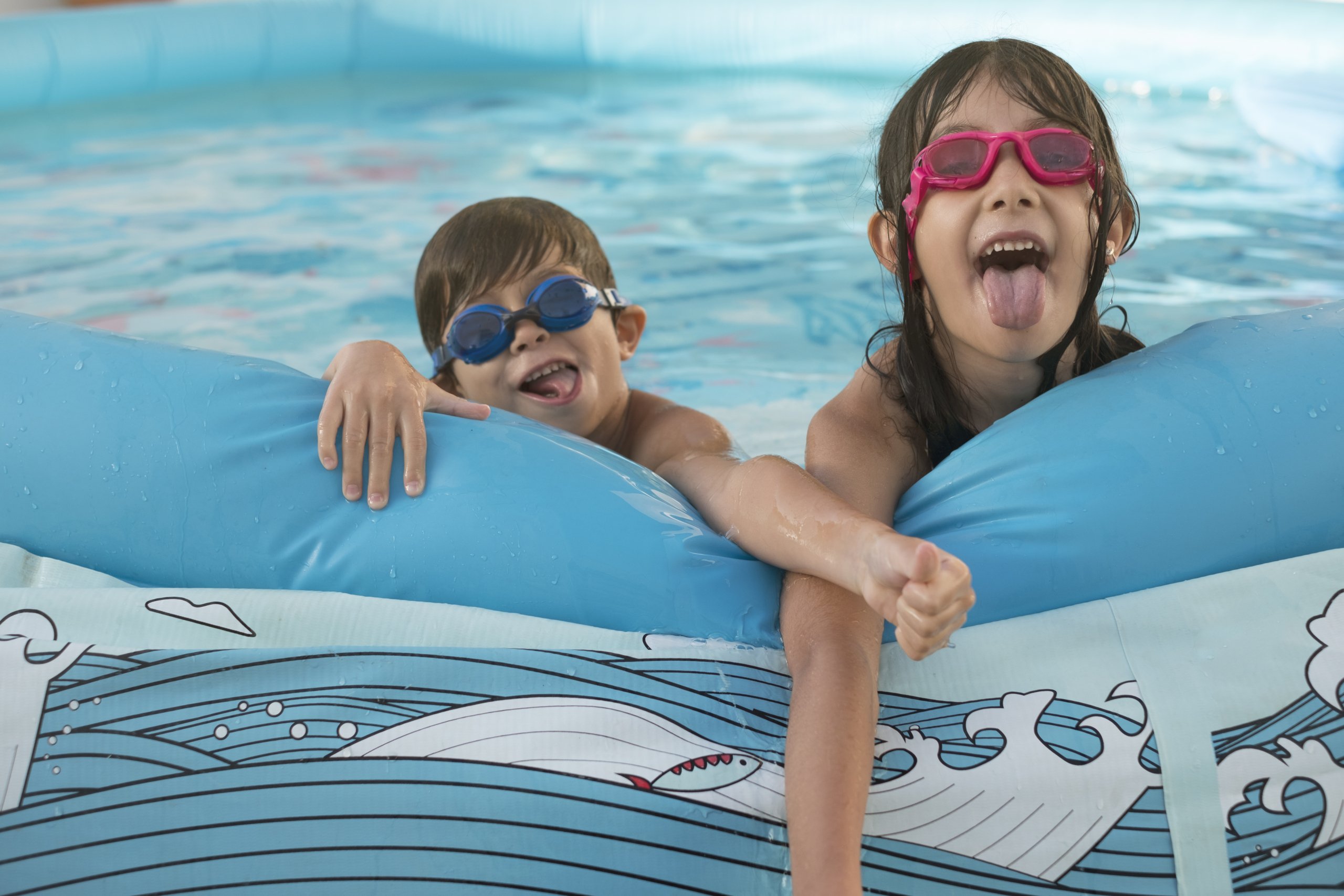 young boy and girl with goggles on playing in a swimming pool