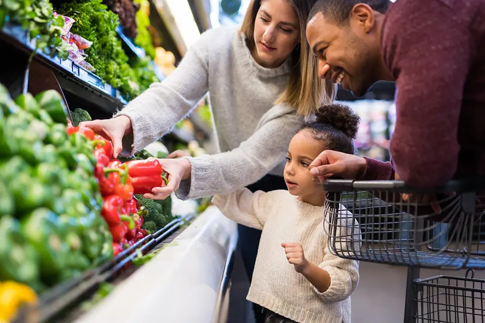 A couple and their toddler carefully choose red bell peppers. 