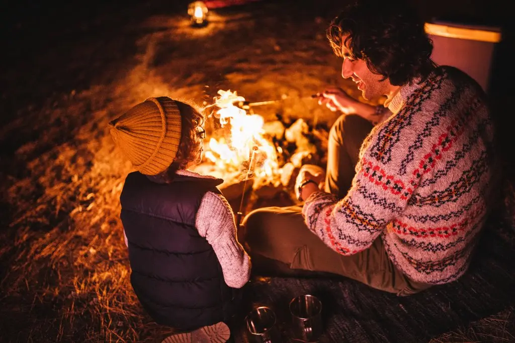 Young father and son camping and roasting marshmallows over bonfire