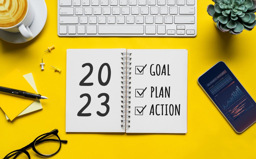 Notebook that reads “2023” on one page and on another page a checklist for “goal”, “plan”, and “action” on top of a desk with office supplies. 