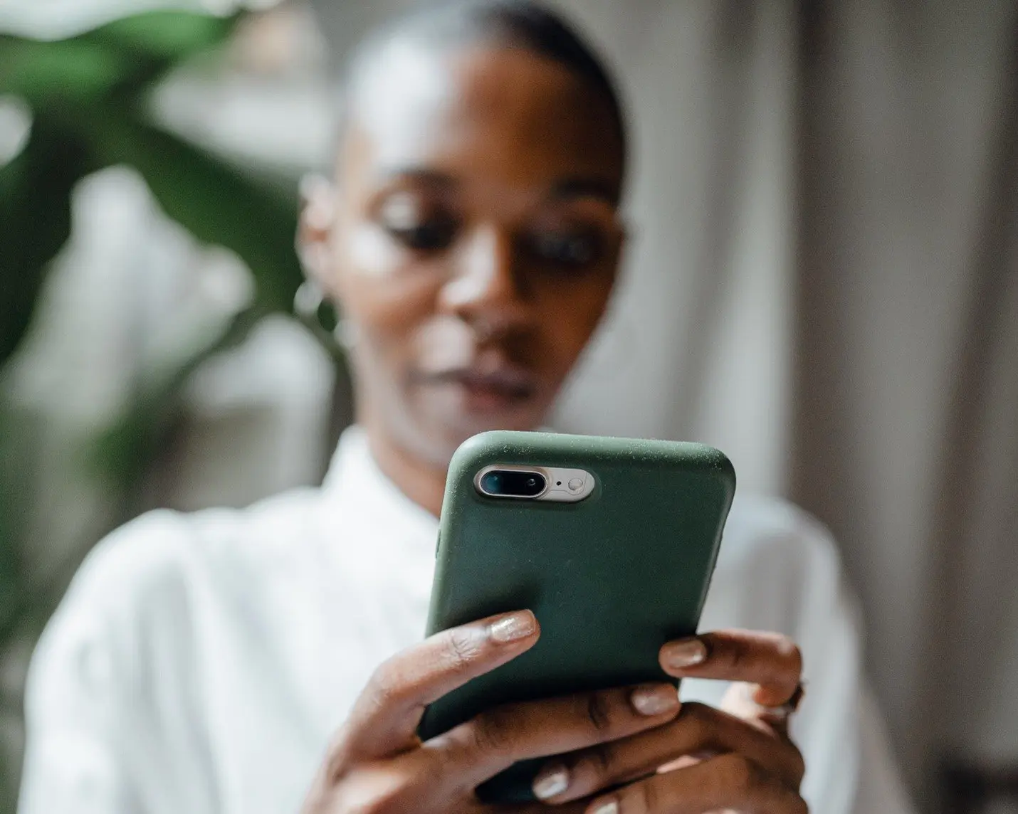 A woman wearing a white shirt holding a green phone, looking at a budgeting app.