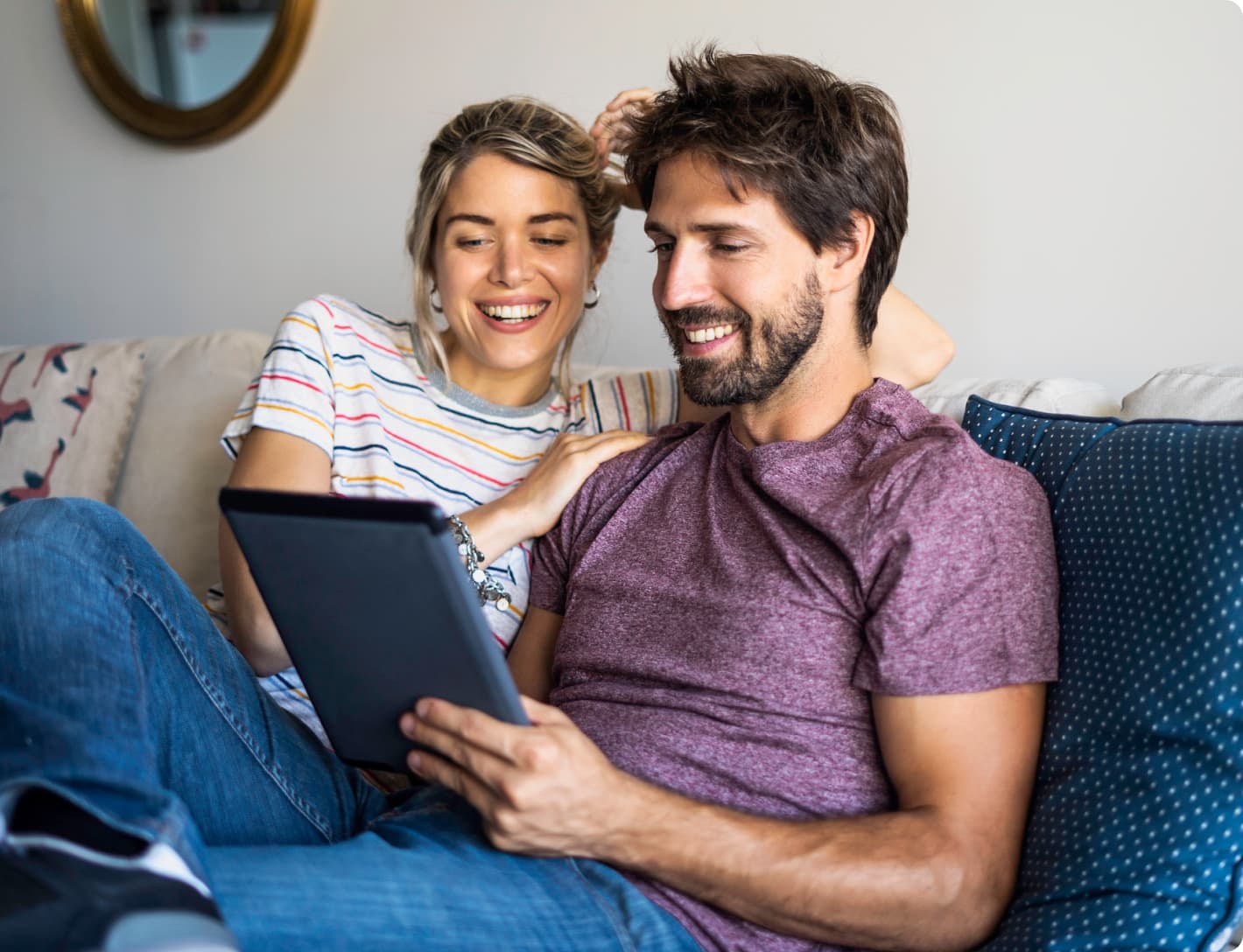 Man and woman on couch smiling and looking at an iPad