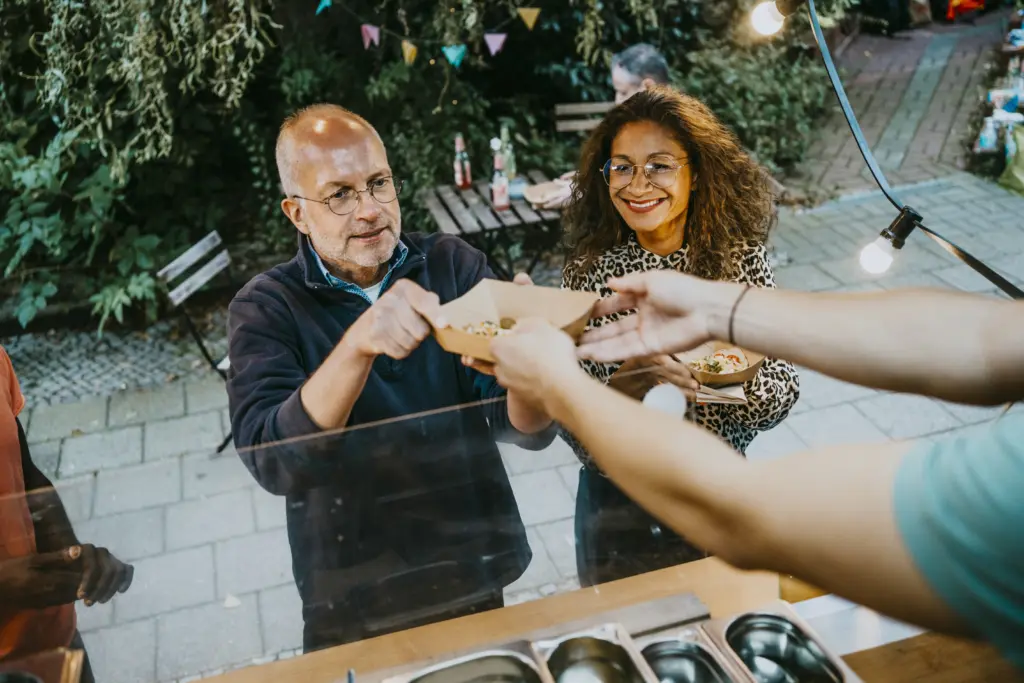 A couple reaches up to accept food from a local vendor in a food truck.