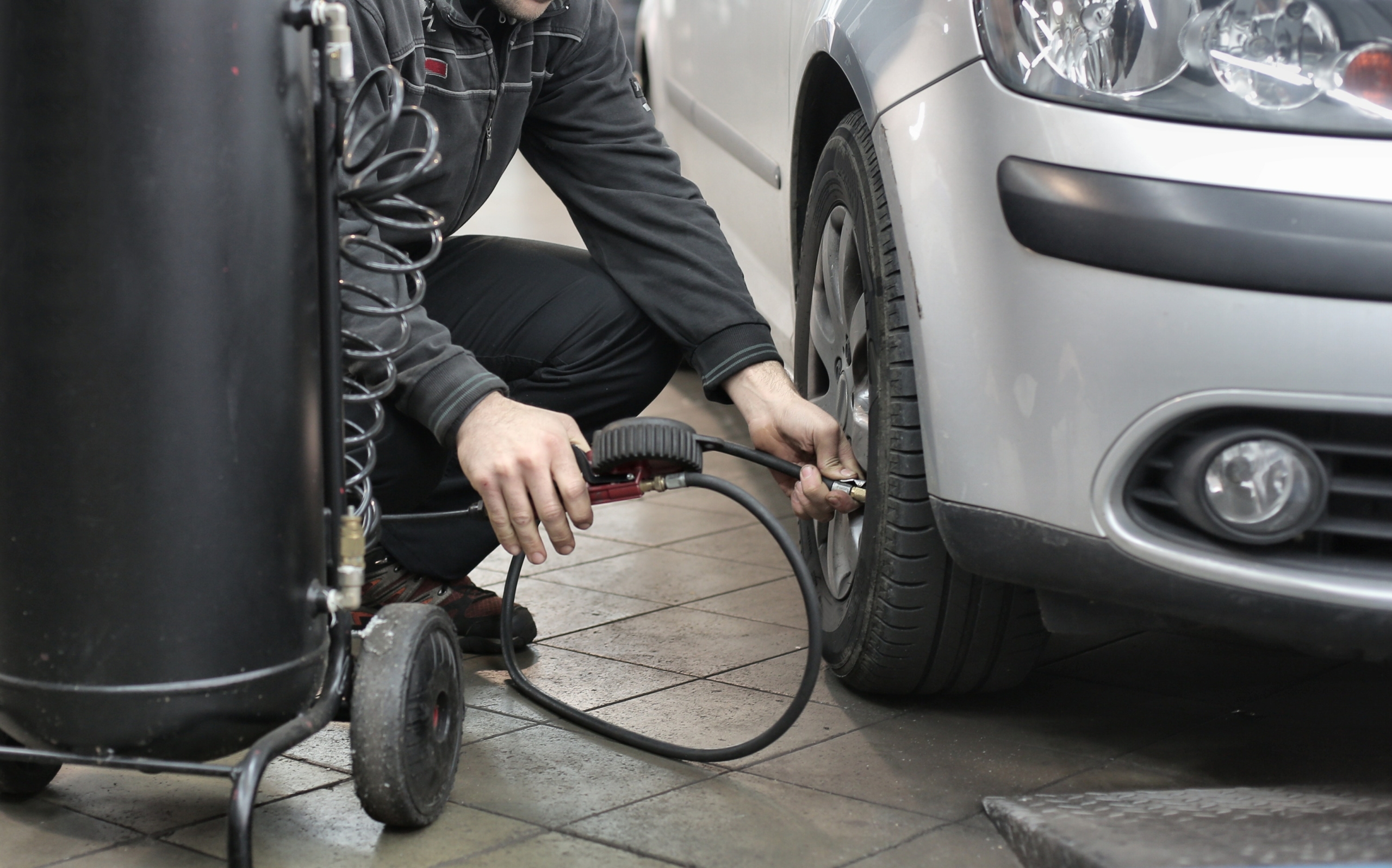 An individual filling their car tire with air as part of their car repair maintenance