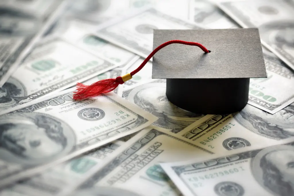 Small Graduation cap sits on top of one hundred dollar bills