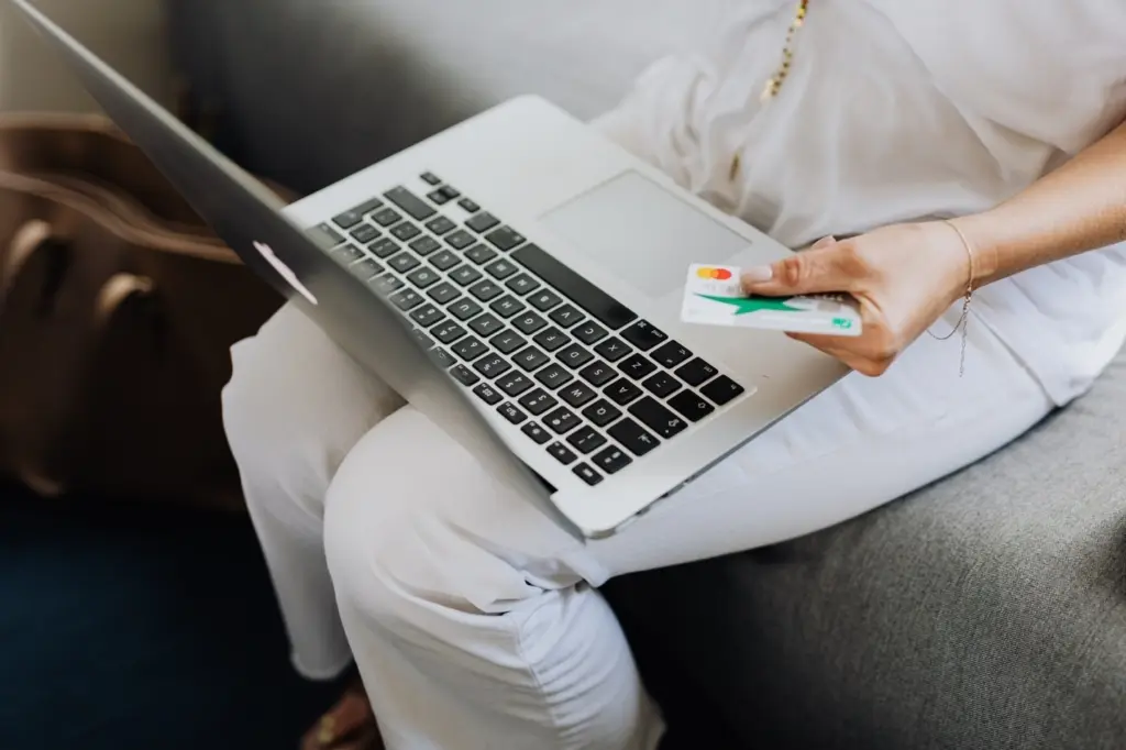 A woman holds a credit card while looking to upgrade debt consolidation on her laptop.