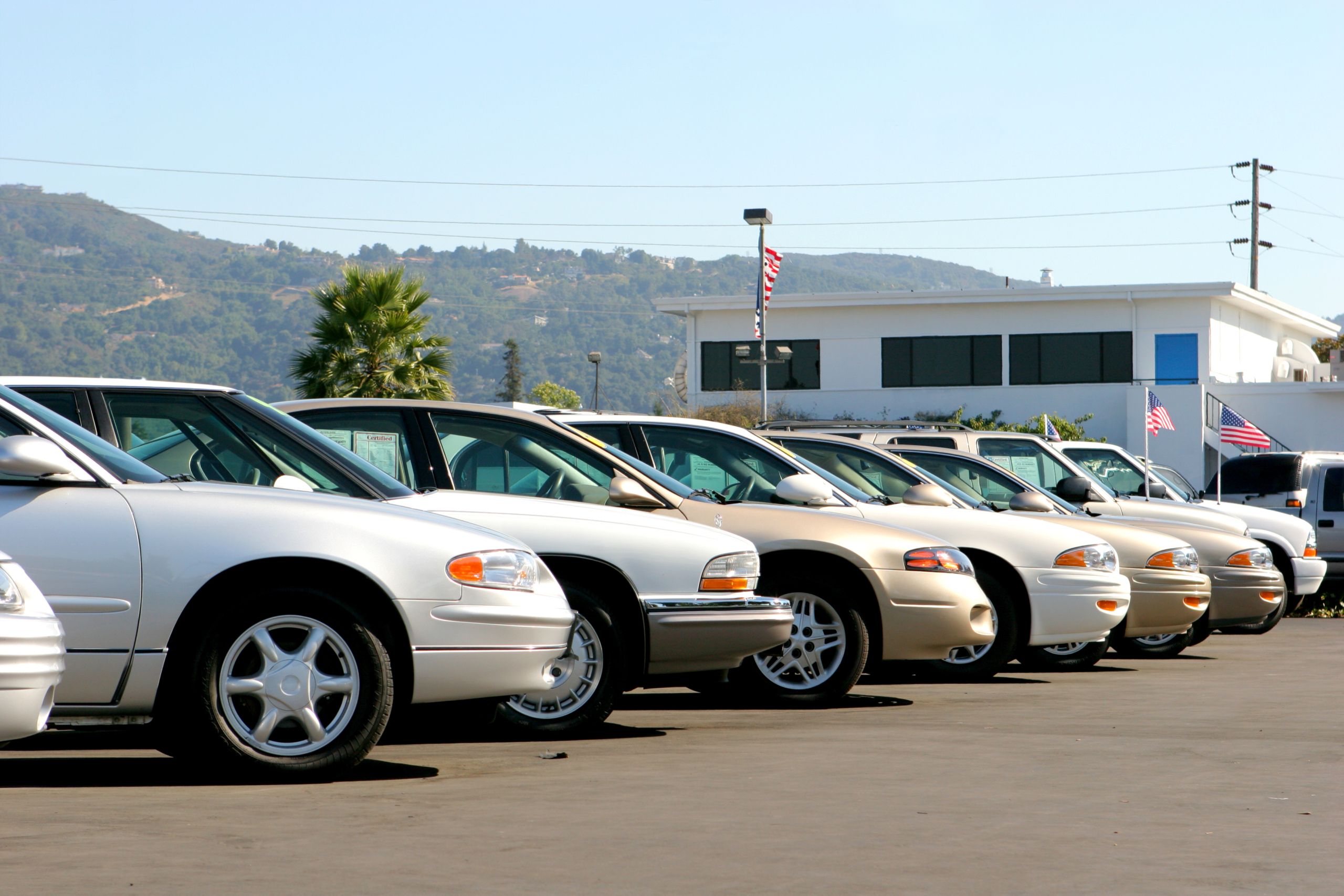A row of used cars at a dealership on a sunny day.