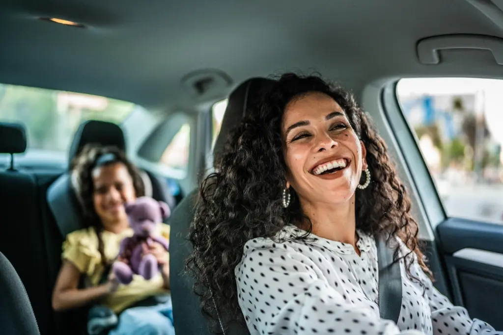 Smiling woman driving a car with a young girl in the backseat