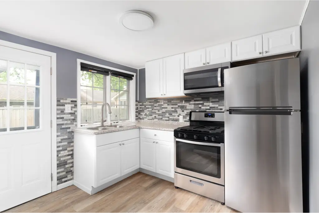 A new kitchen with white cabinetry, hardwood floors, and financed appliances