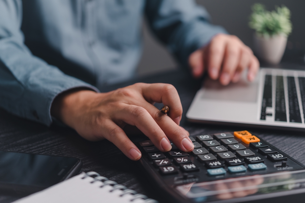 Person using a calculator and laptop to work on financial calculations and refinancing.