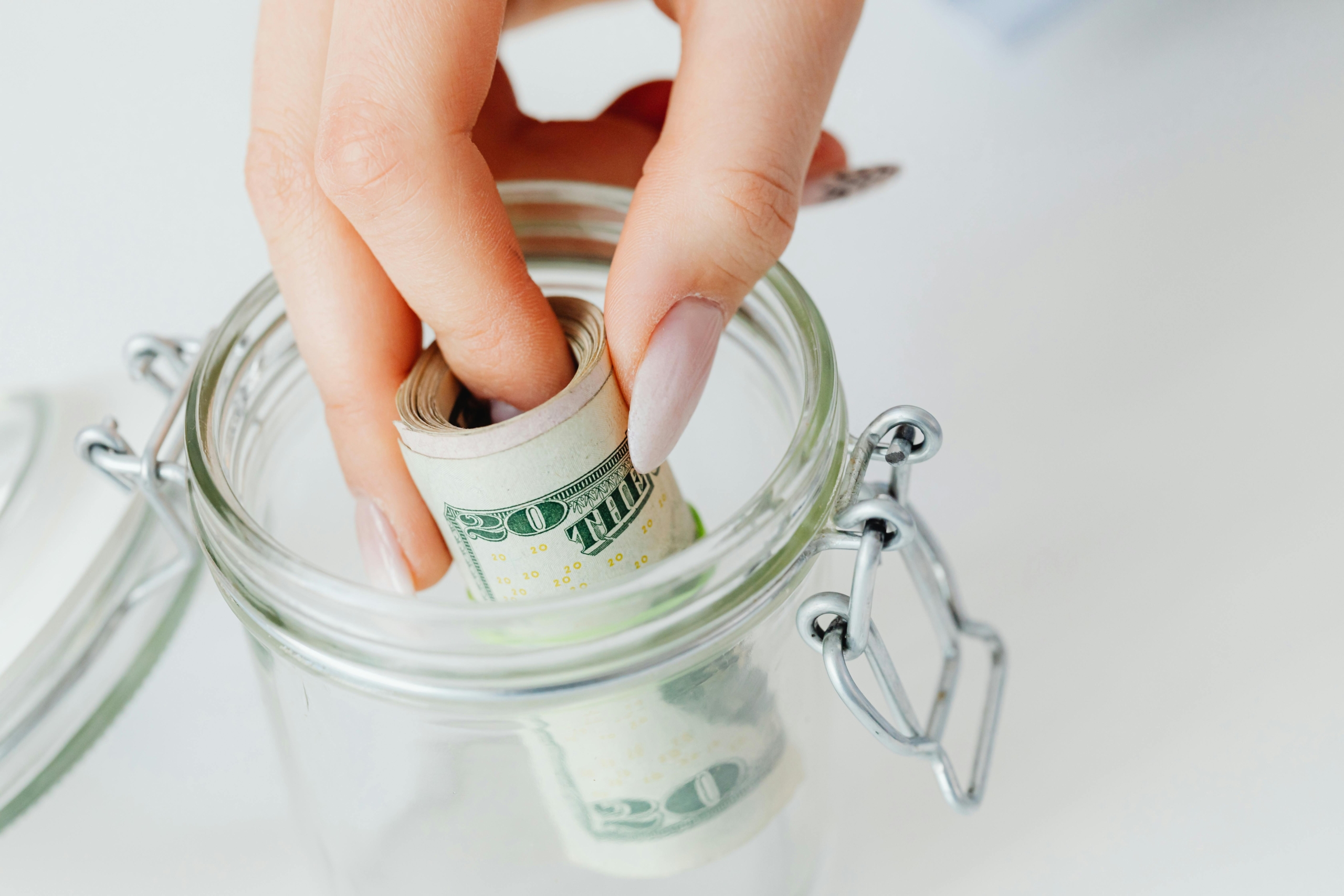 Hand placing rolled cash into a glass jar as an emergency savings fund.