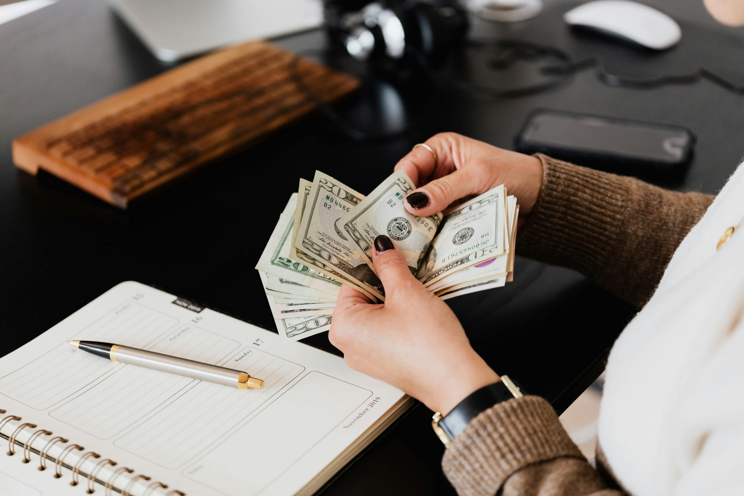 Woman counting cash on her desk, surrounded by bills and coins.