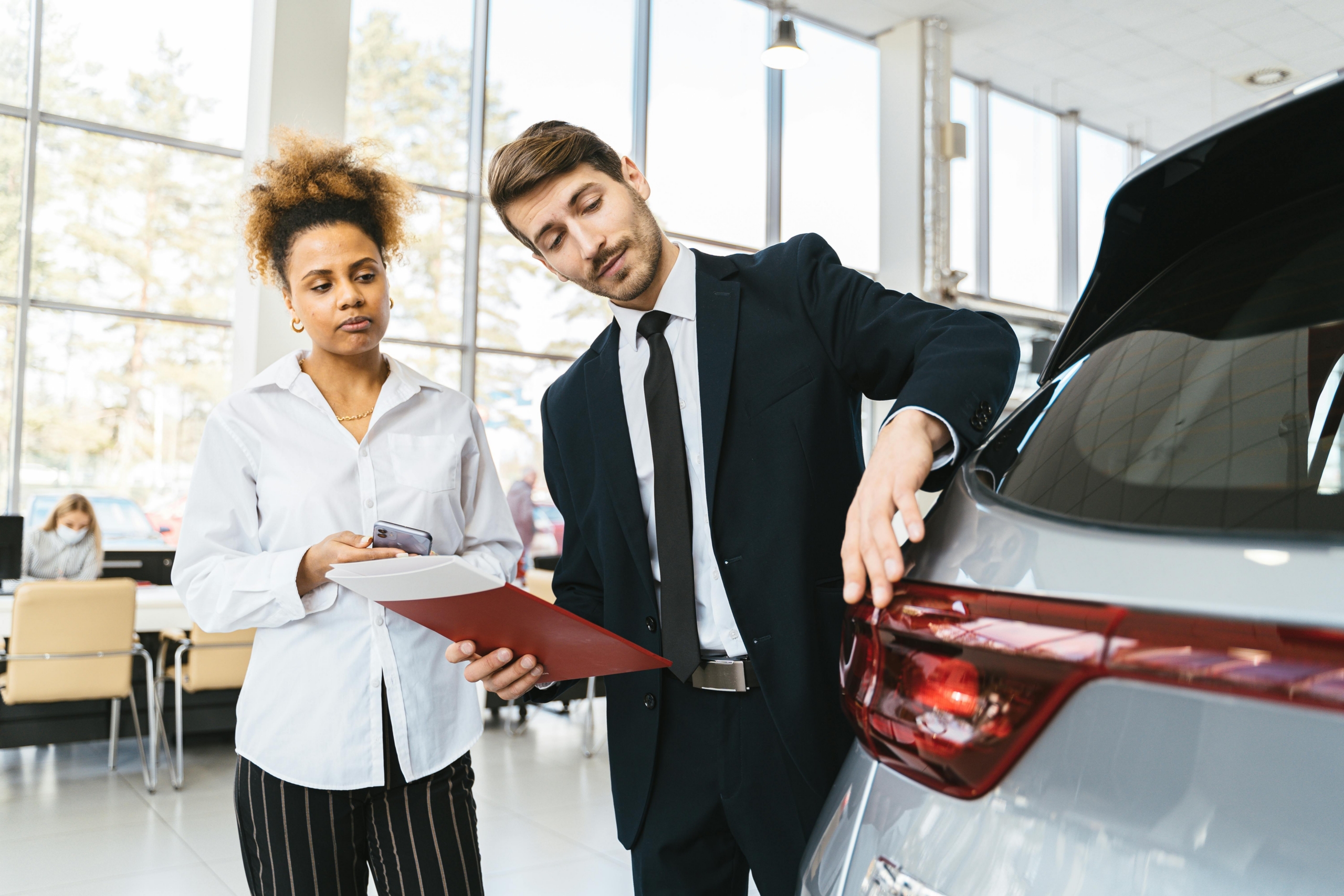 A man and woman in a car dealership, with the woman focused on a car she is interested in buying.