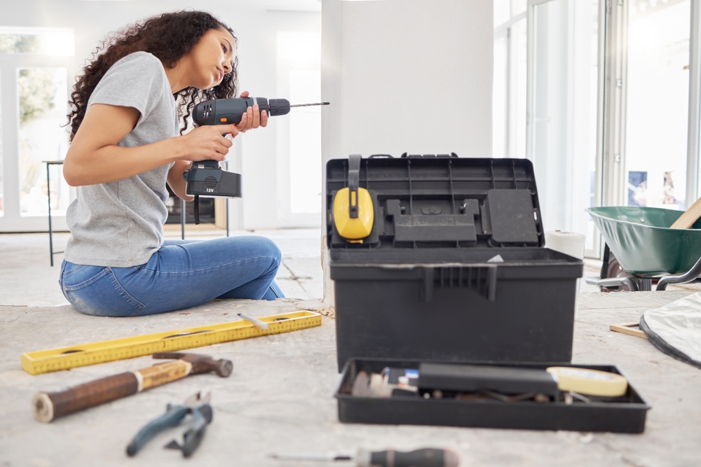 A woman sitting on the floor with a drill performing home maintenance.